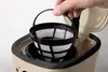 A hand is holding a coffee filter basket over a coffee maker. Náhled obrázku produktu