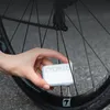 A hand is holding a small white electronic pump next to a bicycle wheel. Náhľad obrázku produktu