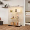 A glass display cabinet with LED lighting is shown in a room with a bed in the background. Produktbild-Vorschau