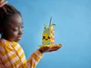 A young girl is holding a colorful LEGO pencil holder made of LEGO bricks in her hand. Podgląd zdjęcia produktu