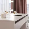A close-up view of a white vanity table with several cosmetic bottles and a candle. Voir les images du produit