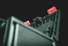 A close-up, low-angle shot of the top of a dark green plastic object, possibly a tool or equipment, with three red plastic clips and a black component visible. Voir les images du produit