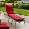 A red chaise lounge cushion on a patio with a grassy area and trees in the background. Produktbild-Vorschau