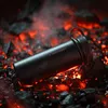 A black thermos bottle is placed on glowing hot coals. Náhled obrázku produktu