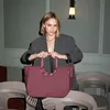 A woman is posing with a handbag in a dimly lit room with chairs. Náhľad obrázku produktu