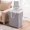 A gray laundry basket is placed next to a beige sofa in a room. Produktbild-Vorschau