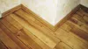 A close-up view of a wooden floor and baseboard in a corner of a room. Produktbild-Vorschau