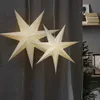 Two white paper star lanterns hang in front of a gray curtain, with a Christmas tree and shelves in the background. Podgląd zdjęcia produktu