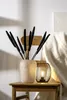 A black lantern with a lit bulb sits on a wooden chair next to a vase of black dried reeds. Anteprima dell’immagine prodotto