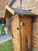 A wooden smoker with a digital control panel and chimney, situated outdoors next to a brick building. Náhled obrázku produktu