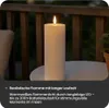 An LED candle with a realistic flame sits on a white table on a balcony at dusk. Produktbild-Vorschau