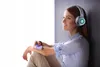 A young woman wearing headphones and holding a smartphone, sitting by a window. Náhľad obrázku produktu