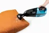 A hand is holding a blue and black handheld vacuum cleaner and using it to clean an orange cushion. Produktbild-Vorschau
