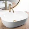 A white oval countertop sink with a gold faucet and drain, placed on a wooden surface, with a round mirror in the background. Anteprima dell’immagine prodotto