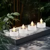 Four white solar LED tea lights with flickering yellow flames are arranged on a gray platform, surrounded by lush green foliage and bamboo stalks. Anteprima dell’immagine prodotto