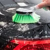 A hand is using a green brush with soap suds to clean a black car. Produktbild-Vorschau