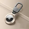 A close-up shot of a golden keychain holder for an Apple AirTag, placed on a light beige and gray background. Produktbild-Vorschau