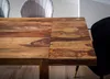 A close-up shot of a wooden dining table with chairs in the background. Produktbild-Vorschau