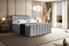 A bedroom scene featuring a large bed with bedding and a bedside table. Produktbild-Vorschau