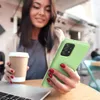 A woman is holding a green phone case and a coffee cup while sitting at a table with a laptop. Produktbild-Vorschau