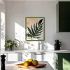 A kitchen counter with a framed picture of a leaf on the wall, a plant, and fruit in a bowl. Produktbild-Vorschau