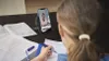 A young girl is studying at a desk, using a smartphone for online learning. Produktbild-Vorschau