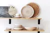 Ceramic tableware and a dried palm leaf are displayed on two wooden shelves against a white wall. Náhled obrázku produktu