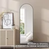 A full-length arched mirror is placed in a room next to a cabinet and a framed picture. Produktbild-Vorschau