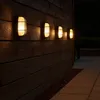 Outdoor wall lights illuminating a wooden wall and patio at night. Produktbild-Vorschau