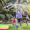 A family is playing with a rocket-shaped sprinkler in a backyard on a sunny day. Produktbild-Vorschau