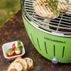 A close-up of a green LotusGrill charcoal grill with food and bread on a wooden surface. Náhled obrázku produktu