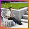A man is sitting in a white hammock chair outdoors, working on a laptop. Produktbild-Vorschau