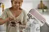 A woman is adding ingredients to a stand mixer in a kitchen. Voir les images du produit