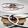 A close-up view of a modern ceiling lamp with multiple rings, showing its adjustable features and a wood-like base. Produktbild-Vorschau