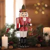 A festive Christmas scene featuring a nutcracker figurine surrounded by pine branches, candles, and walnuts. Podgląd zdjęcia produktu