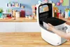 A person is using a white deep fryer in a kitchen setting. The background shows kitchen shelves with various items. Produktbild-Vorschau