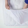 A person's hands are shown tucking a white mattress protector onto a mattress. Anteprima dell’immagine prodotto