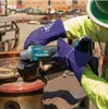 A person is using a Makita angle grinder on a metal object in an outdoor construction or industrial setting. Produktbild-Vorschau