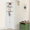 A white corner cabinet with louvered doors and open shelves, decorated with various items, stands in a room with framed artwork on the wall and a green side table. Produktbild-Vorschau