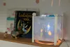 A night light with a projection of stars and a character from The Little Prince is displayed on a shelf next to books and small figurines. Produktbild-Vorschau