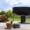 A small dog lies on a wooden deck next to a pile of firewood and a large black fire pit. Produktbild-Vorschau