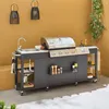 An outdoor kitchen setup with a gas grill, sink, and storage cabinets against a yellow wall. Produktbild-Vorschau