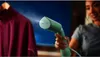A person is steaming a maroon garment with a green handheld steamer. Produktbild-Vorschau
