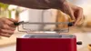 A person's hands are shown placing a wire rack onto a red toaster. Voir les images du produit