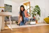 A woman is cleaning a rug with a Kärcher washing vacuum cleaner in a living room. Produktbild-Vorschau