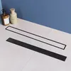 Two black shower drains are displayed on a tiled surface in front of a blue wall. Two bottles of soap or lotion are in the background. Produktbild-Vorschau