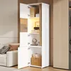 A tall, white cabinet with wood accents, open doors revealing shelves with decorative items and books, set in a living room next to a sofa. Anteprima dell’immagine prodotto