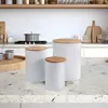 A kitchen counter with three white storage canisters with wooden lids. Produktbild-Vorschau