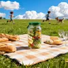 Transparentes Glas-Salatglas mit grünem Deckel, gefüllt mit geschichteten Gemüsen, auf einer karierten Picknickdecke mit Baguettes und Käse Podgląd zdjęcia produktu