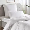 A close-up view of white bedding, including a large pillow and a smaller pillow, on a bed with a grey headboard. Produktbild-Vorschau